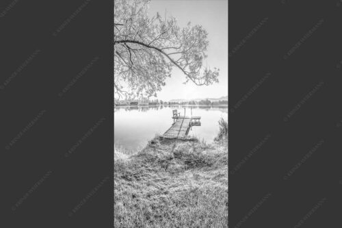 Blick über den Kochelsee bei Schlehdorf in den Sonnenaufgang - Die Sonne geht immer wieder auf III 1:2 sw -- Bootssteg mit Bank am Kochelsee - mehr Infos bei www.Kriner-Weiermann.de